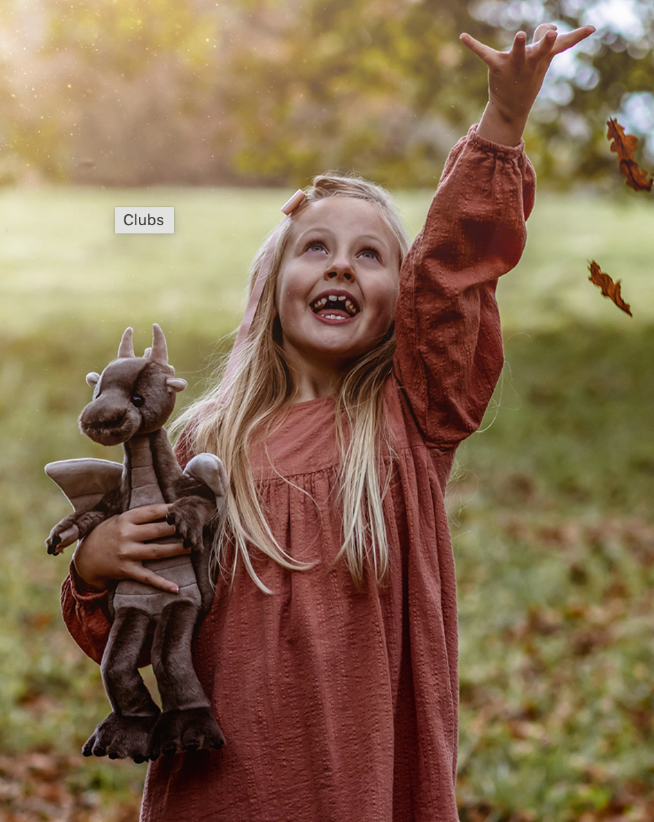 Young girl in a pink dress holding a dragon toy outdoors with leaves falling around her.