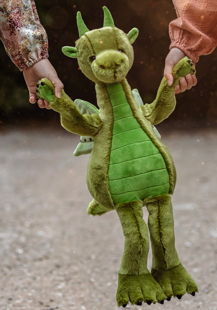 Green plush dragon toy held by two hands on a blurred background