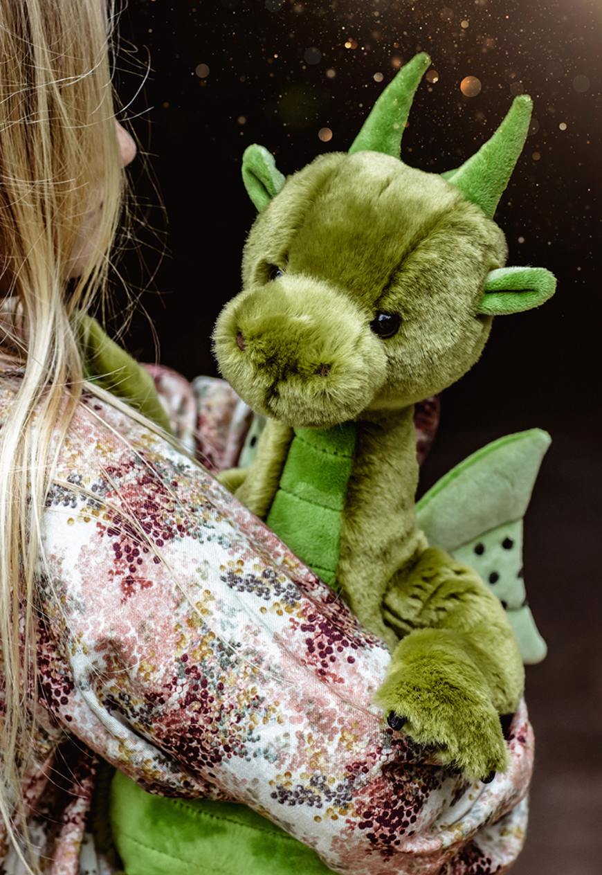 Green plush dragon toy held by a person with a dark background