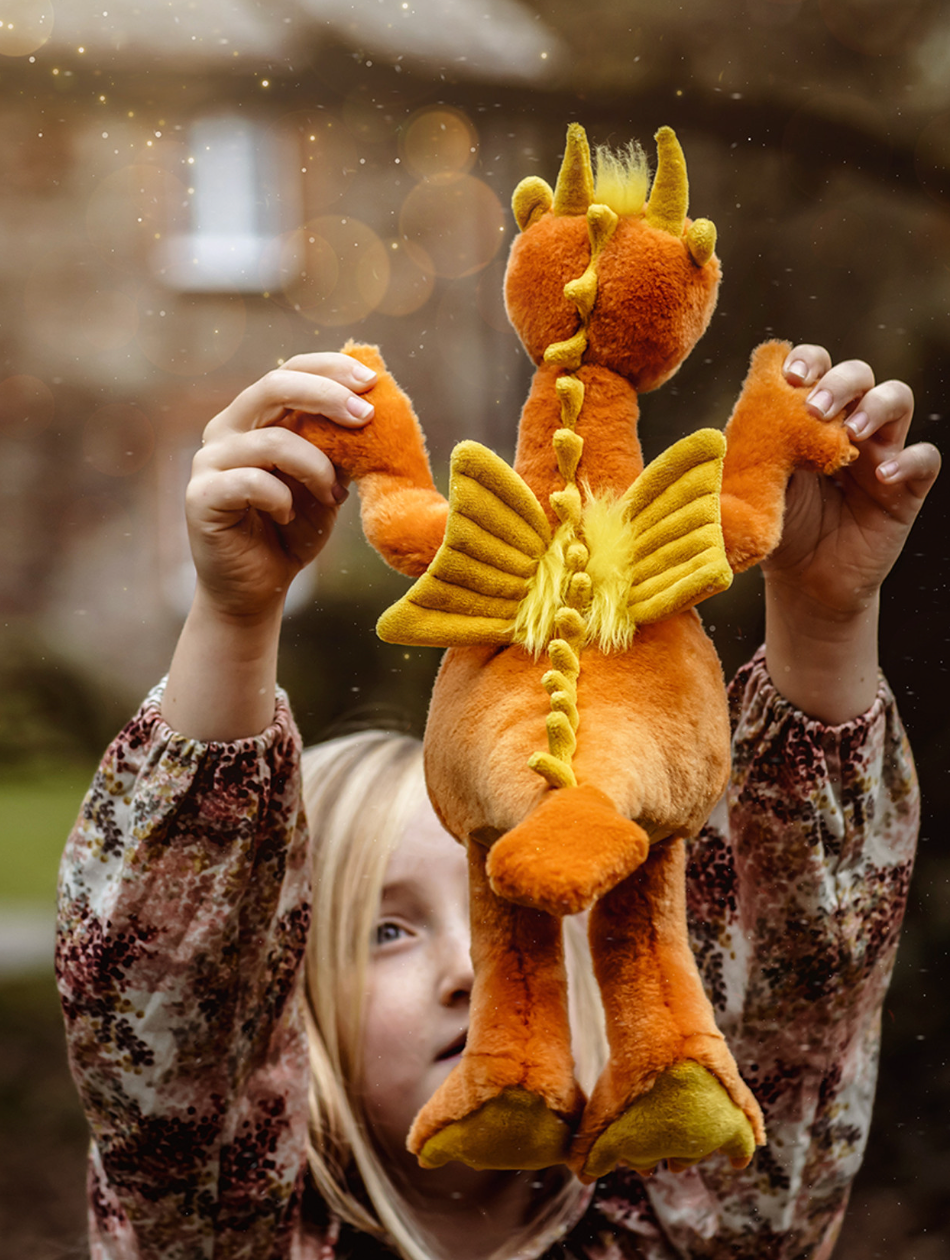 Child holding a plush dragon toy with a blurred outdoor background