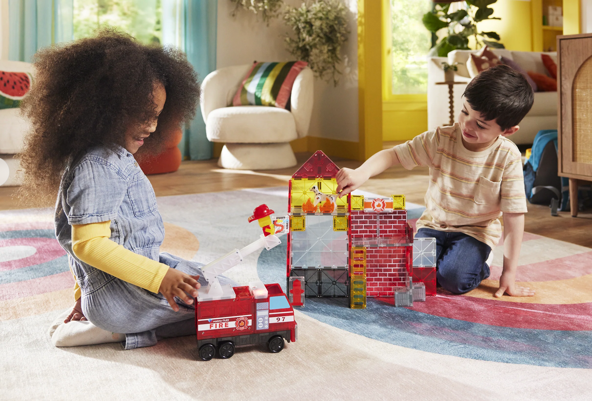 Two children playing with toy fire truck and building set in a living room.