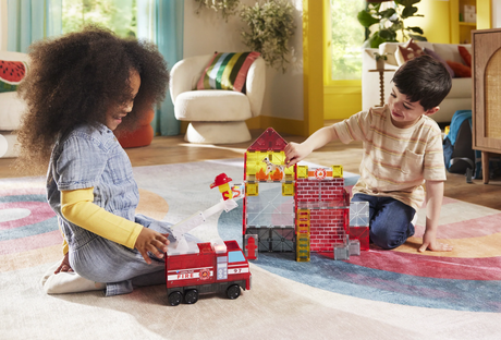 Two children playing with toy fire truck and building set in a living room.