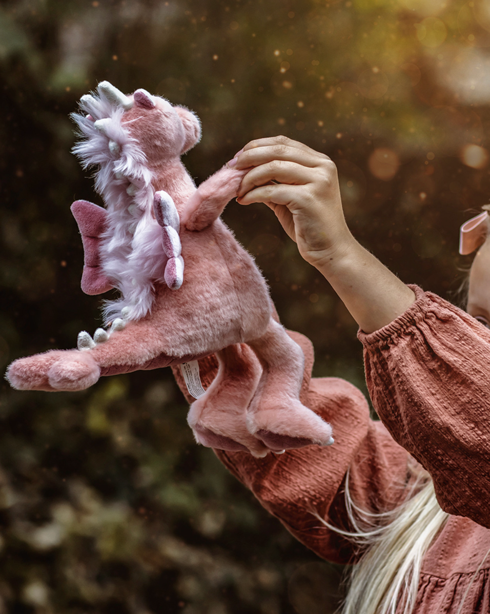 Person holding a pink dragon plush toy against a blurred natural background