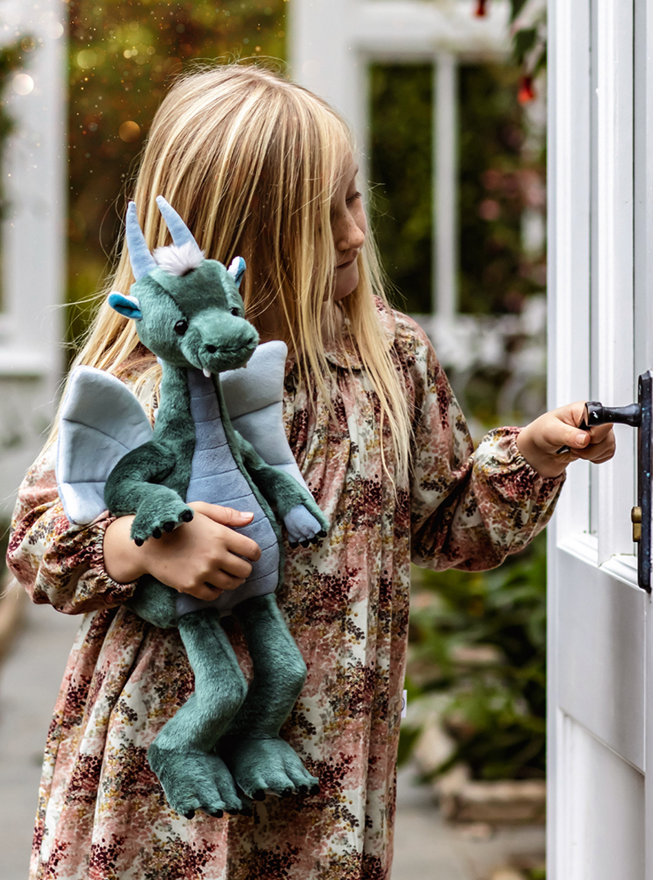 Child holding a plush dragon toy in front of a door